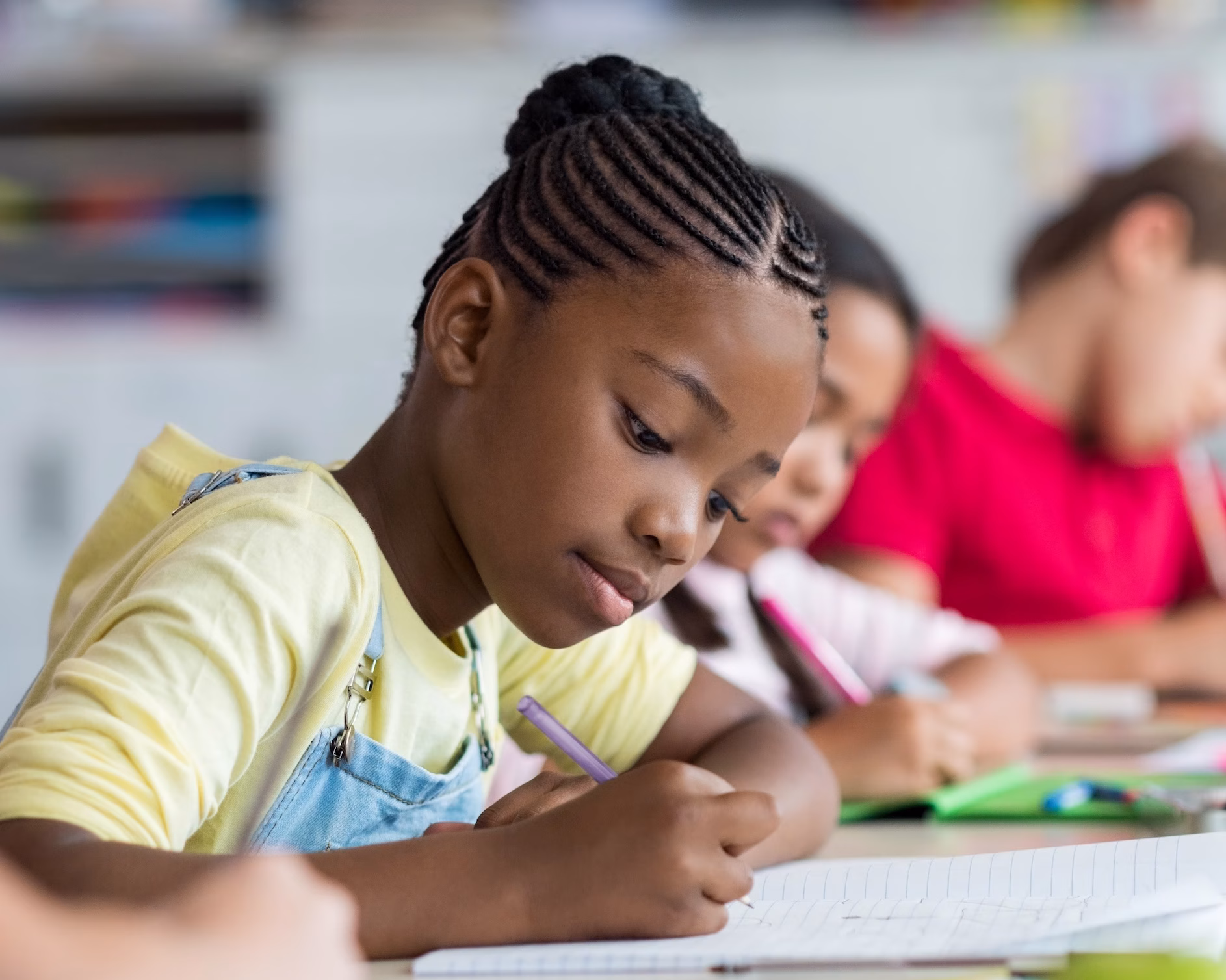 Cute pupil writing at desk in classroom at the elementary school. Student girl doing test in primary school. Children writing notes in classroom. African schoolgirl writing on notebook during the lesson.